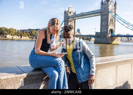 Smiling woman sharing smart phone with friend near Tower bridge in city Stock Photo