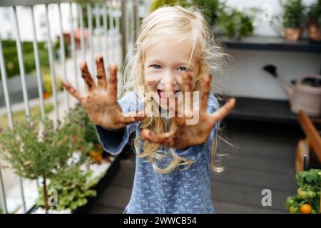 Cheerful girl showing hands covered in dirt at balcony garden Stock Photo