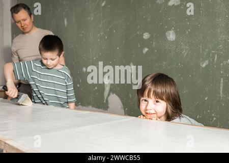 Smiling boy leaning on workbench by father and brother applying glue on wallpaper Stock Photo
