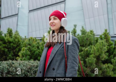Smiling woman wearing wireless headphones and standing near plants Stock Photo