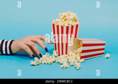 Hand of woman reaching for popcorn over blue background Stock Photo