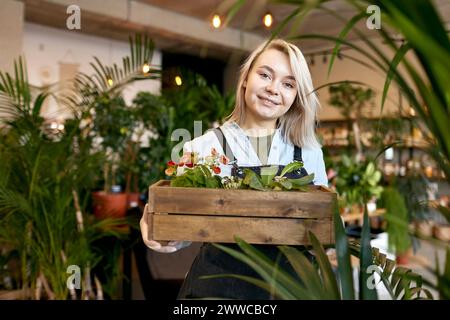 Happy gardener holding crate of plants in garden center Stock Photo