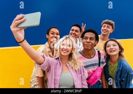 Laughing multi-ethnic friends taking smartphone selfie in front of yellow wall Stock Photo