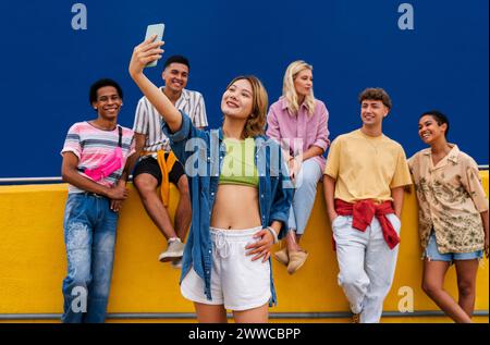 Confident young woman standing in front of group of friends taking a selfie Stock Photo