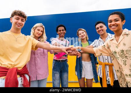 Multi-ethnic group of young friends stacking hands in front of wall Stock Photo