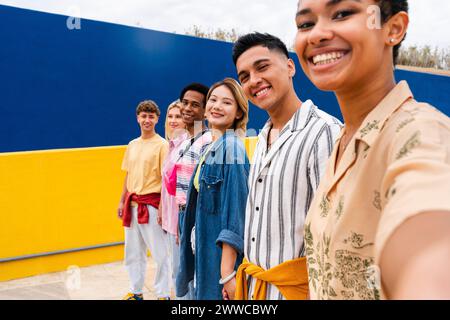 Multi-ethnic group of young friends standing smiling in front of colorful wall Stock Photo