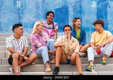 Multi ethnic group of young people sitting on steps in front of wall Stock Photo