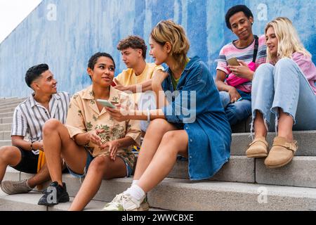 Happy group of young people using smartphones on steps in front of wall Stock Photo