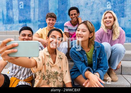Happy group of young people taking selfie on steps in front of wall Stock Photo