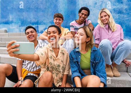 Happy group of young people taking selfie on steps in front of wall Stock Photo