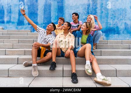 Happy group of young people taking selfie on steps in front of wall Stock Photo