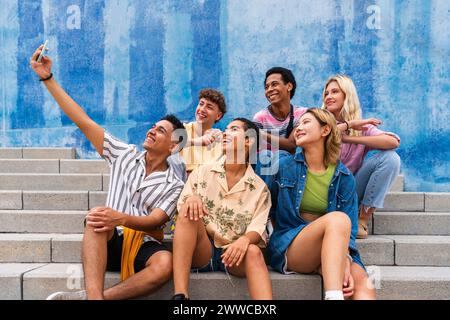 Happy group of young people taking selfie on steps in front of wall Stock Photo