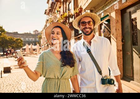 Happy woman holding smart phone with man on street near buildings Stock Photo