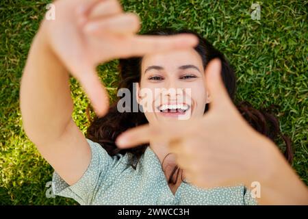 Happy woman looking through finger frame and lying on grass Stock Photo