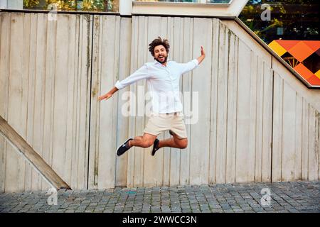Happy young man jumping in front of wall Stock Photo