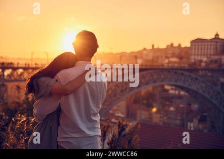 Young couple embracing each other in front of Dom Luis bridge at sunset, Porto, Portugal Stock Photo