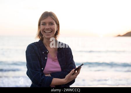 Cheerful woman holding smart phone at sunset beach Stock Photo