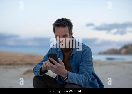 Man using smart phone at sunset beach Stock Photo