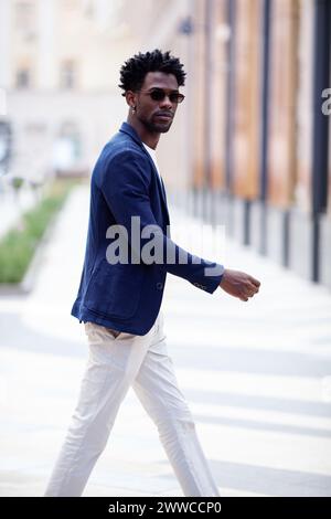 Handsome fashion African American man walks down the street in stylish attire white pants, blue blazer. Fashionable street style trend for men. Stock Photo