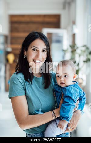 Happy mother carrying baby girl in living room at home Stock Photo