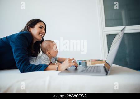 Businesswoman lying with baby girl using laptop on bed at home Stock Photo