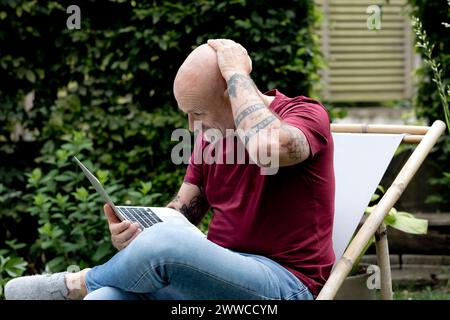 Confused freelancer with head in hand using laptop in garden Stock Photo