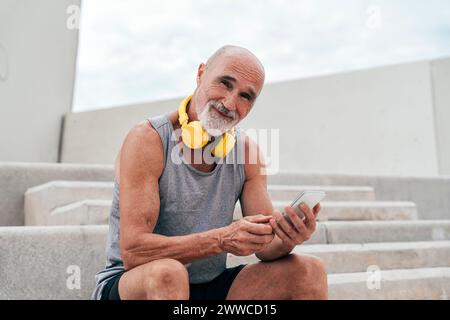 Smiling retired senior man using smart phone sitting on staircase Stock Photo