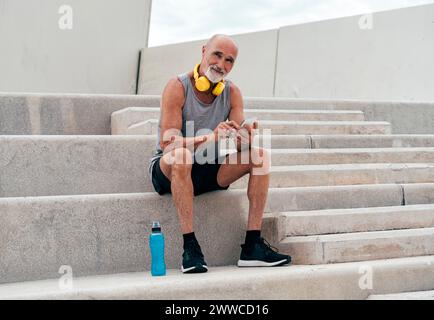 Retired senior man using smart phone sitting on staircase Stock Photo