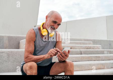 Smiling senior man using smart phone sitting on staircase Stock Photo