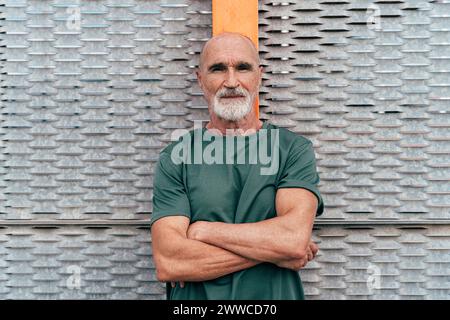 Senior man with arms crossed leaning on fence Stock Photo