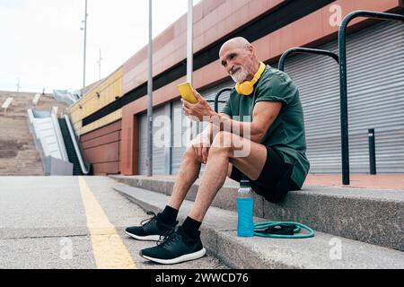 Smiling senior man using smart phone sitting on steps Stock Photo