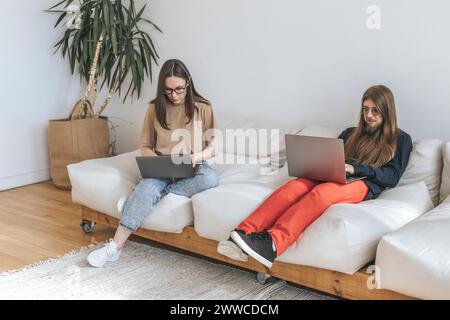Programmers sitting on sofa coding through laptops at creative office Stock Photo