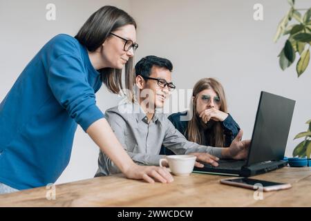 Smiling programmer discussing coding on laptop with colleagues at startup Stock Photo