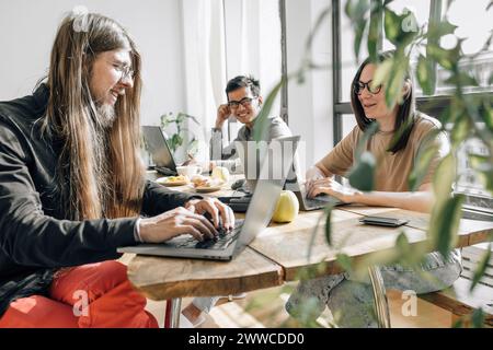Team of IT technicians sitting at table coding on laptops in office Stock Photo
