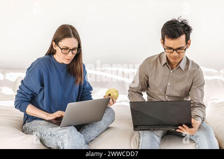 Diverse programmers using laptops sitting on sofa at creative startup office Stock Photo