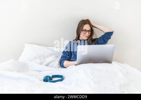 Programmer using laptop sitting on bed at home Stock Photo