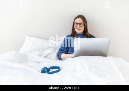 Smiling programmer using laptop sitting on bed at home Stock Photo