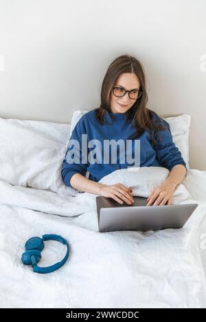 Smiling programmer coding through laptop sitting on bed at home Stock Photo