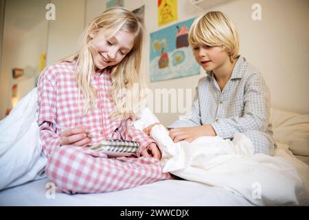 Brother with sister writing in book sitting on bed at home Stock Photo