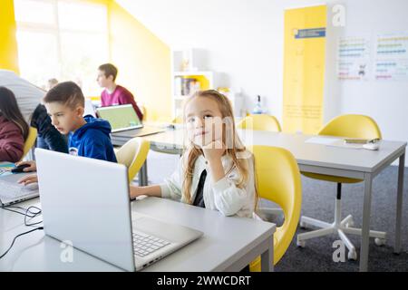 Girl sitting with hand on chin using laptop in computer classroom at school Stock Photo