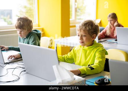 Blond boys using laptops learning computer coding in classroom Stock Photo