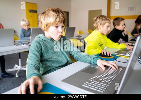 Blond boy using laptop learning computer programming at desk Stock Photo