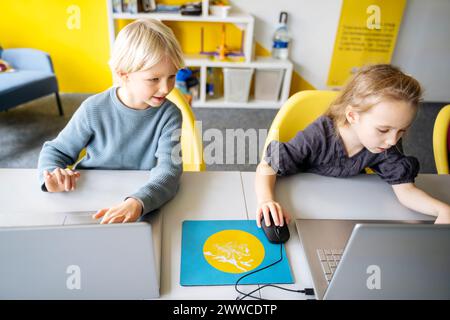 Boy and girl sitting at desk with laptops learning computers in classroom Stock Photo
