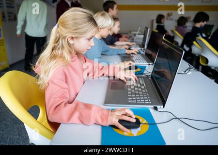 Dedicated blond girl using laptop learning computer at desk in classroom Stock Photo