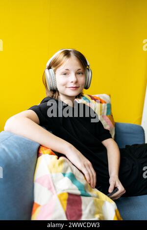 Smiling girl sitting on sofa listening to music in school Stock Photo