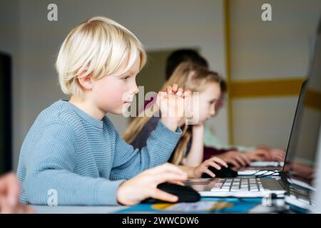 Blond boy learning coding through laptop desk in classroom Stock Photo