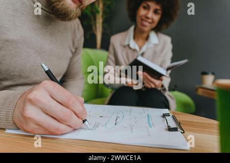 Businessman planning strategy on clipboard sitting by businesswoman in office Stock Photo