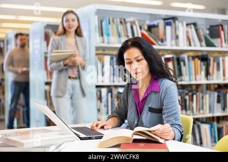 Focused woman working on laptop at library Stock Photo