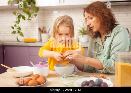 Grandmother and granddaughter cook in kitchen in middle, family pastime, leisure. woman and child make cake in purple, lavender kitchen. plum pie Stock Photo