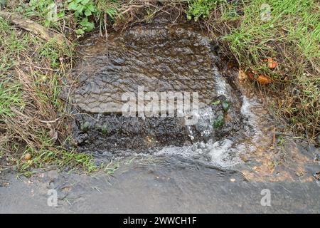 Slough, UK. 21st March, 2024. Water has been flowing out of a manhole cover in Dropmore Road in Slough for months now. Potholes in the road await repair. Credit: Maureen McLean/Alamy Stock Photo